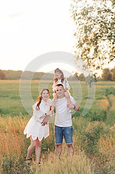 Family walks on meadow and father carries daughter on his shoulders