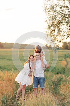 Family walks on meadow and father carries daughter on his shoulders