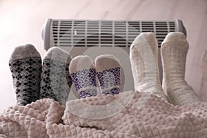 Family warming feet near electric heater at home, closeup
