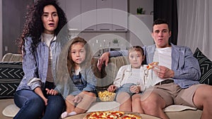 Family watches horror movie together and eats pizza on sofa