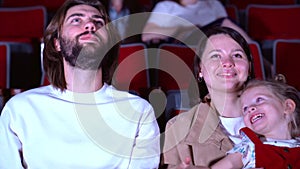 Family watching film in cinema. Media. Portrait of happy mom, dad, and cure little girl sitting together and watching an