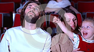 Family watching film in cinema. Media. Portrait of happy mom, dad, and cure little girl sitting together and watching an