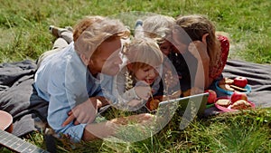 Family watching tablet computer on picnic lying green grass. Summer vacation.