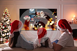 Family watching TV movie in room decorated for Christmas, back view
