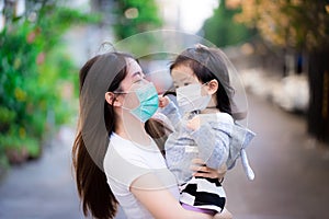 Family wear face mask stood embracing each other on street. Mother smiles at her daughter under medical mask.