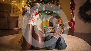 Family wearing knitted wool socks relaxing on carpet and looking on christmas tree decorated with colorful garland