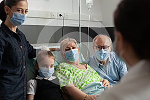Family wearing protective face mask against coronavirus while visiting elderly senior woman