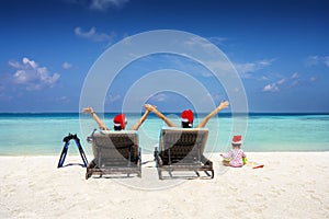 A family wearing santa claus hats sits in sunbeds on a tropical beach