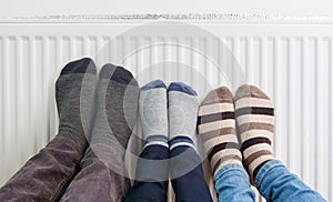 Family wears colorful pair of woolly socks warming cold feet in front of heating radiator in winter time.