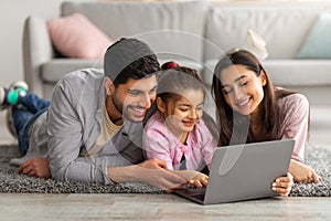 Family weekend. Cheerful arab parents teaching their little daughter using laptop, spending time at home together