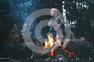 Family weekend outdoor. Cute curious child near bonfire in forest. Local travel, camping, hiking lifestyle