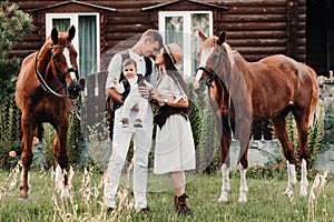 A family in white clothes with their son stand near two beautiful horses in nature. A stylish couple with a child are photographed