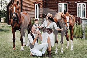 A family in white clothes with their son stand near two beautiful horses in nature. A stylish couple with a child are photographed