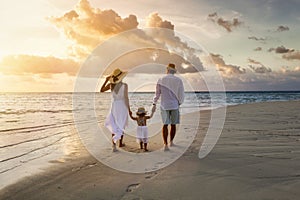A family in white summer clothing walks hand in hand down a tropical paradise beach during sunset tme