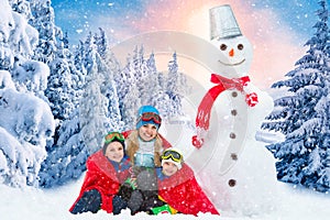 A family in a winter snowy forest mold a big snowman.Family winter fun for Christmas vacation.