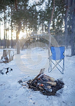 Family winter picnic. Bonfire and camping chair, winter walk in snowy forest on weekend, vertical