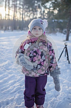 Family winter picnic. Little girl sits by campfire in snow-covered forest, active weekend