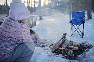 Family winter picnic. Little girl sits by campfire in snow-covered forest, active weekend