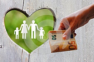 Family on wooden background with green heart and money in hand