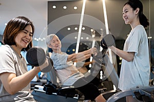 Family workout in the gym,smiling asian mother and daughter exercise with dumbbells,senior grandmother sit on the spinning bicycle