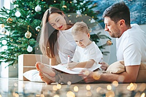Family writing a letter to Santa Claus near the Christmas tree