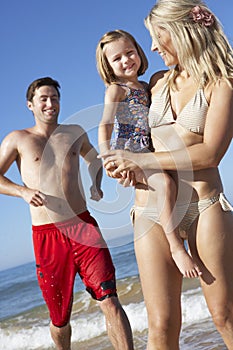 Family With Young Daughter Running Along Beach Together