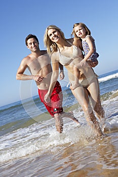 Family With Young Daughter Running Along Beach Together