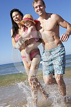 Family With Young Daughter Running Along Beach Together