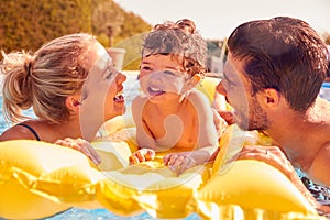 Family With Young Son Having Fun With Inflatable On Summer Vacation In Outdoor Swimming Pool