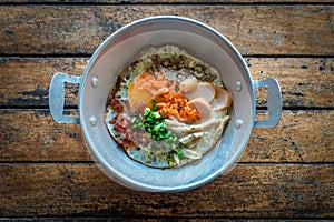 The famous breakfast thai food Panned eggs is fried egg topping with sausage, vegetable and bacon in the hot pan on wooden table