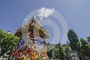 The famous clock tower, one of the city of Graz attractions, made of flowers and the real Clock Tower Grazer Uhrturm in the