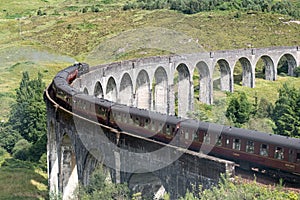 Famous Glenfinnan Viaduct in Scotland with a historic steam train and tourists with motion blur effect