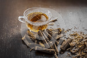 Famous herb Licorice root or Liquorice root or Mulethi root on wooden surface along with its beneficial tea in a transparent cup.