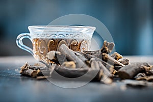 Famous herb Licorice root or Liquorice root or Mulethi root on wooden surface along with its beneficial tea in a transparent cup.