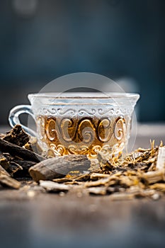 Famous herb Licorice root or Liquorice root or Mulethi root on wooden surface along with its beneficial tea in a transparent cup.