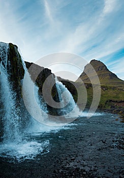 Famous icelandic waterfalls with looming Kirkjufell arrowhead mountain in background