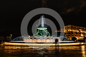 Famous illuminated Tritons Fountain at night,three bronze mythological Tritons sculptures holding up huge basin,modern landmark of