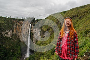 The famous Indonesia Sipiso Piso waterfall on Toba Lake, among the jungle and European young Caucasian girl tourist photo