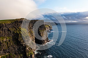 Famous Irish cliffs of Moher in west coast of Ireland with calm and sea water under a cloudy white and blue sky during