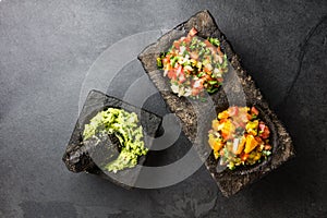 Famous mexican sauces salsas - pico de gallo, avocado guacamole, salsa bandera mexicana in stone mortars on gray slate background photo