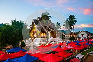 Famous night market in Luang Prabang, Laos with illuminated temple and sunset sky