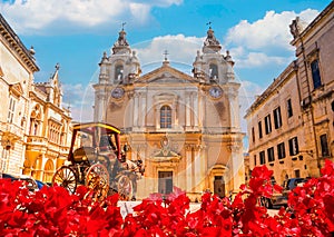 The famous Saint Paul Cathedral architecture in Mdina surrounded by red flowers