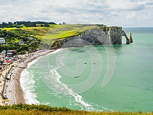 Famous view of Etretat coastline, green fields and vertical chalk cliffs with characteristic arch and pinnacle, Normandy, France