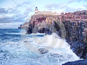 Famous view to Neist Point lighthouse on the end of world. Foamy sea strikes against cliffs.