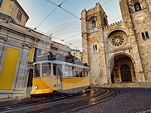 A famous yellow tram 28 passing in front of Santa Maria cathedral in Lisbon, Portugal at dusk or twilight