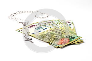 Fan of 500 Argentine pesos banknotes next to Catholic rosary isolated on white background