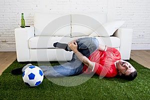 Fanatic football fan on green grass carpet emulating soccer stadium pitch mocking player in pain hurt on ankle