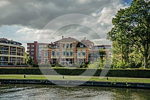 Fancy brick building next to wide tree-lined canal under cloudy sky at sunset in Weesp.