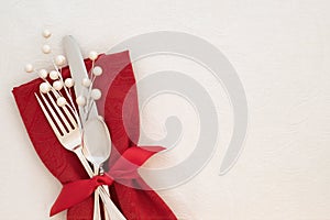 Fancy Christmas Table Place Setting with red napkin, silverware, and white berries on creamy white tablecloth background with copy