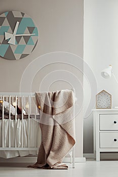 Fancy clack on the wall of elegant baby bedroom interior with white wooden crib with pastel pink blanket and cotton ball lights